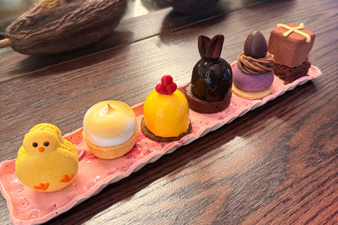 Easter mini cakes arrangement on a pink base and chocolate pieces on a wooden surface.